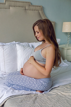 pregnant girl in bra and pants sitting on bed in studioの写真素材