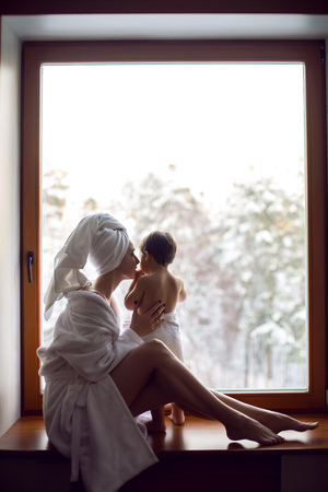 mom and son sitting by the window on a wide windowsill in a bathrobe after a bathの写真素材