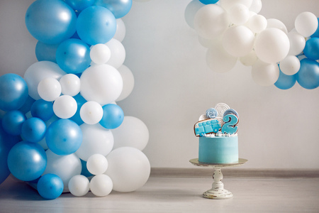 blue cake on childrens birthday with the number two and a car on the background of balloonsの写真素材