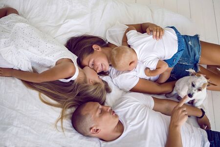 happy family lying on a big white bed in a room with a dog