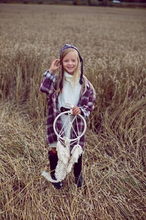 blonde girl in white in a dress and boots goes with a dream catcher in a wheat fieldの写真素材