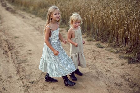 two girls in long dresses walk along the path to the field of dry wheatの写真素材