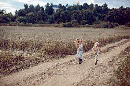 two girls in long dresses running along the path to the field of dry wheatの写真素材