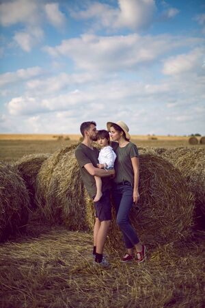 family mom dad son stand in a sloping field near the haystacks summerの写真素材