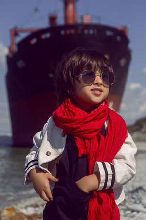 fashionable boy child with long hair dance next to a large ship that ran aground near Novorossiysk