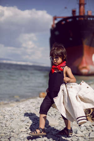 fashionable boy child with long hair stand on a log next to a large ship that ran aground near Novorossiyskの写真素材