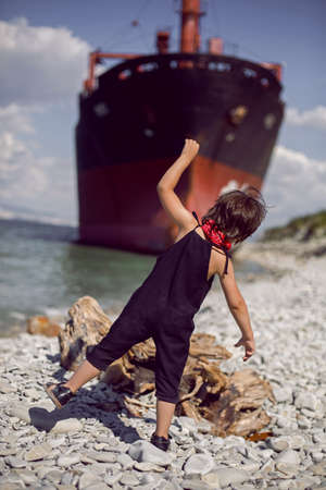 fashionable boy child with long hair stand on a log next to a large ship that ran aground near Novorossiyskの写真素材