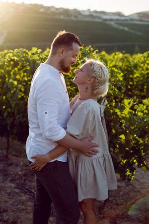 man and a woman in white clothes stand in a grape field at sunsetの写真素材