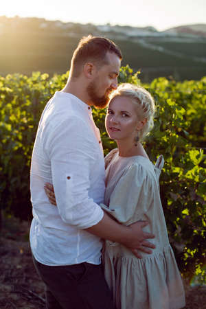 man and a woman in white clothes stand in a grape field at sunsetの写真素材