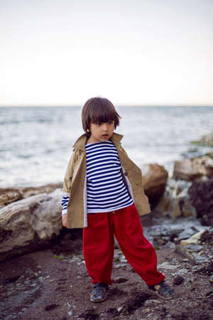 stylish boy sailor in a vest and red pants stands on the seashore in summerの写真素材