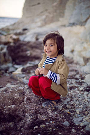 stylish boy sailor in a vest and red pants sit on the seashore in summerの写真素材