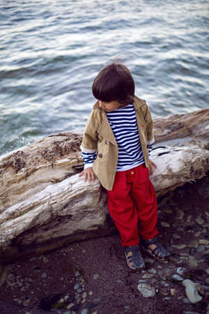 stylish boy sailor in a vest and red pants sit on the seashore in summerの写真素材