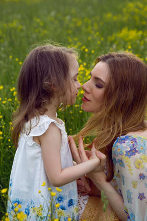mother and daughter in dresses and a hat stand in a field of yellow flowers in the summer dayの写真素材