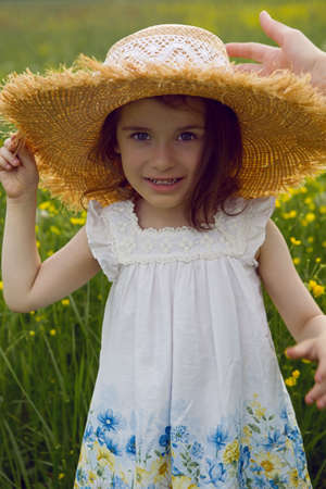 child girl in a straw hat and a dress with flowers stands on a yellow fieldの写真素材