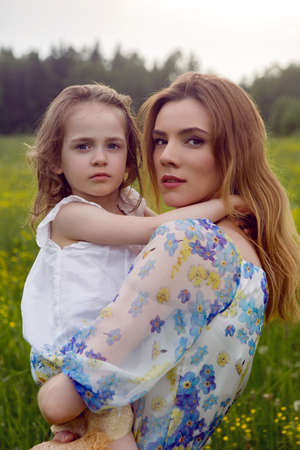 mother and daughter in dresses and a hat stand in a field of yellow flowers in the summer dayの写真素材