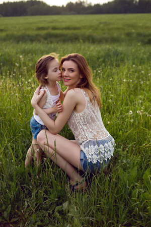 mom and daughter are sitting in a green field in white t-shirtの写真素材