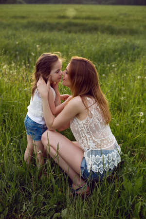 mom and daughter are sitting in a green field in white t-shirtの写真素材