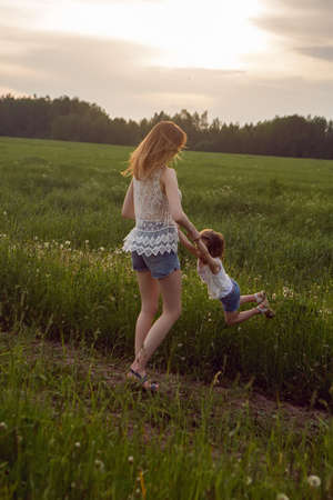 mom and daughter in white t-shirts and denim shorts have fun on a green field in summerの写真素材