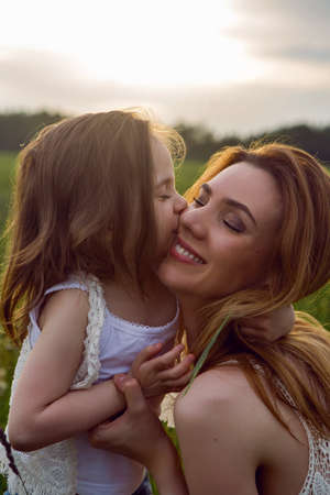 mom and daughter are sitting in a green field in white t-shirtの写真素材