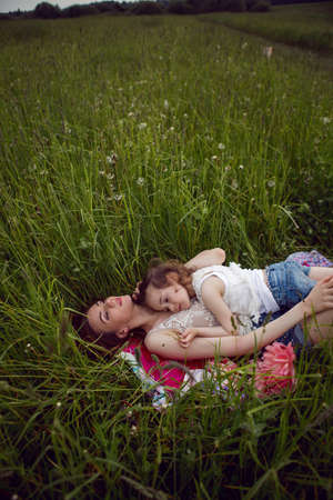 mother and daughter lie on a green field in summer and relax in the sunの写真素材