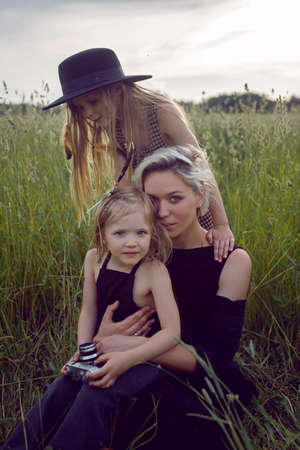 mother in an evening dress and a retro camera with two daughters on a green field with grass in the summerの写真素材