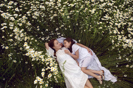 mother with daughter in a white dress lie on a camomile fieldの写真素材