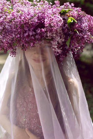 Caucasian girl child seven years old in a purple dress stands in nature with a wreath of lilacsの写真素材