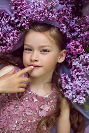 child girl in a purple floral dress lies on the ground among lilacs on a veil in springの写真素材
