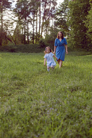 mother and daughter walk along the field with dandelions in blue dressesの写真素材