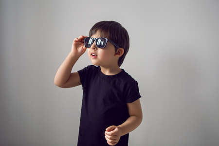boy in a black t-shirt stands at home against the background of a white room in sunglasses ,during quarantine and thinks about traveling to countriesの写真素材