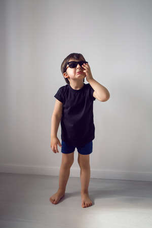 boy in a black t-shirt stands at home against the background of a white room in sunglasses ,during quarantine and thinks about traveling to countriesの写真素材