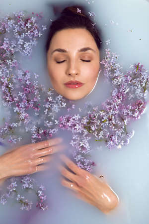 woman lies in a white bath with milk and lilac flowersの写真素材
