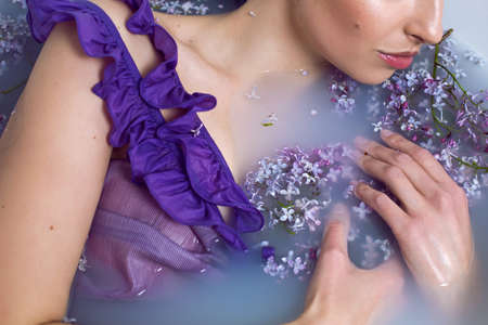 sexy fashionable woman in swimsuit dress lies in a white bath with milk and lilac flowersの写真素材