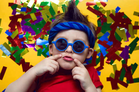 child a boy in a red t shirt and sunglasses is lying on yellow paper resting at home during the...