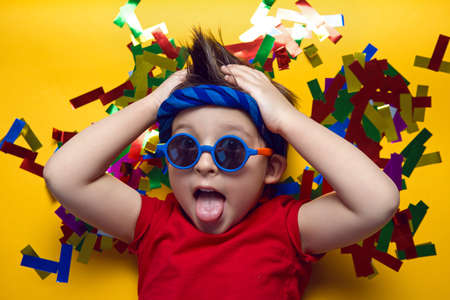 child a boy in a red t shirt and sunglasses is lying on yellow paper resting at home during the epidemicの写真素材