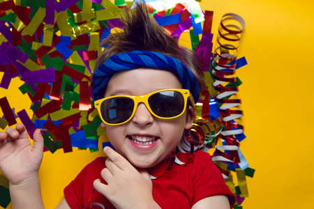 child a boy in a red t shirt and sunglasses is lying on yellow paper resting at home during the epidemicの写真素材