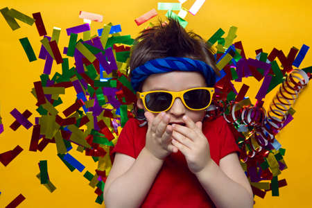 child a boy in a red t shirt and sunglasses is lying on yellow paper resting at home during the epidemicの写真素材