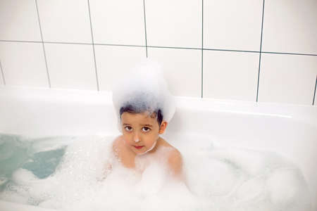boy with big eyes a Caucasian child bathes in a white bath with foamの写真素材