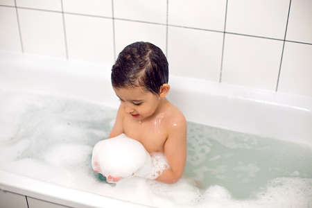 boy with big eyes a Caucasian child bathes in a white bath with foamの写真素材