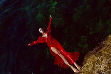woman swims in the sea in a red long dress with sunglasses in summerの写真素材