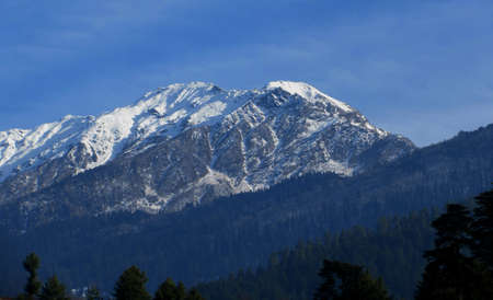 Dark blue Sky with snow-covered mountains and tall trees in Himachal Pradesh Indiaの写真素材