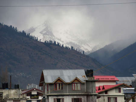 Dark cloudy Sky with snow-covered mountains and tall trees in Himachal Pradesh Indiaの写真素材