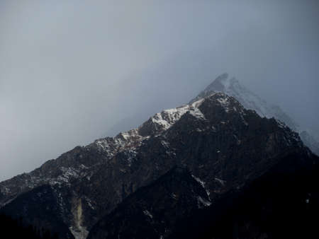 Dark cloudy Sky with snow-covered mountains and tall trees in Himachal Pradesh Indiaの写真素材