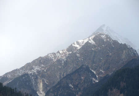 Dark cloudy Sky with snow-covered mountains and tall trees in Himachal Pradesh Indiaの写真素材