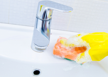 woman doing chores in bathroom at home cleaning sink and faucet with spray detergentの写真素材