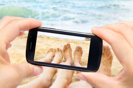 Hands taking photo legs in sea with smartphoneの写真素材