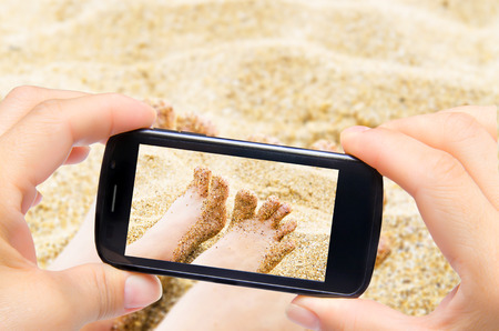 Hands taking photo girl legs in sea with smartphoneの写真素材