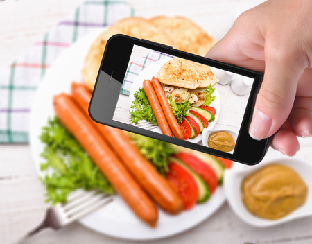 Hands taking photo sausages and vegetables with smartphoneの写真素材