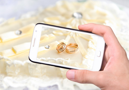 Hands taking photo wedding rings with smartphoneの写真素材