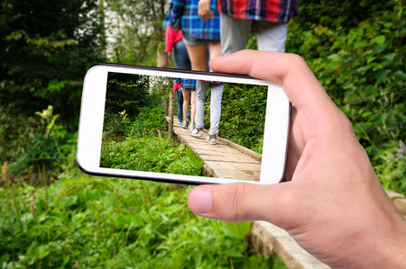 Hands taking photo tourists walking on a wooden bridge with smartphone.の写真素材